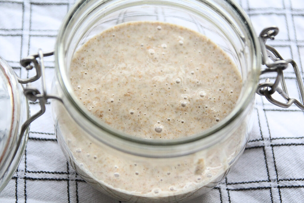 Zuurdesemstarter met bubbels in pot op theedoek.