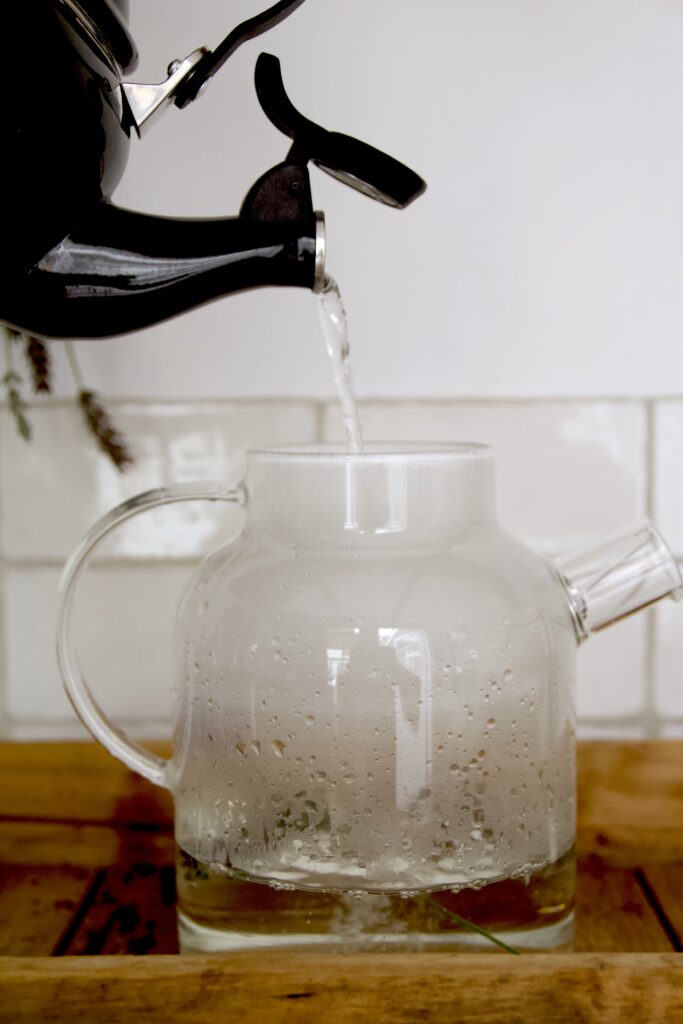 Heet water gieten bij lavendel in glazen theepot